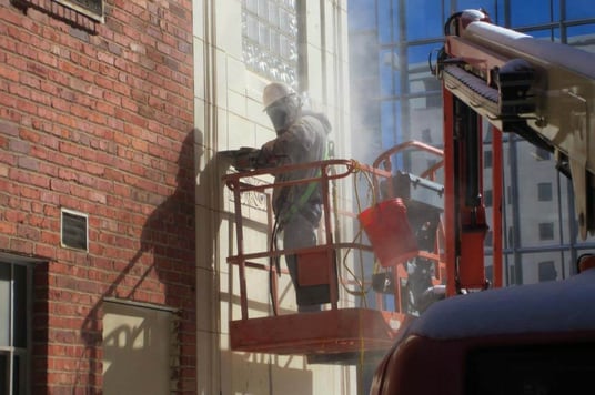 Worker in a protective suit is standing in a crane working on the side of a building located in Oklahoma City